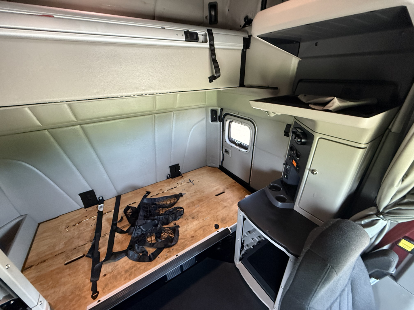 Peterbilt 579 truck interior cargo area with wooden floor, seat, storage cabinet, and window seen from sleeper area.