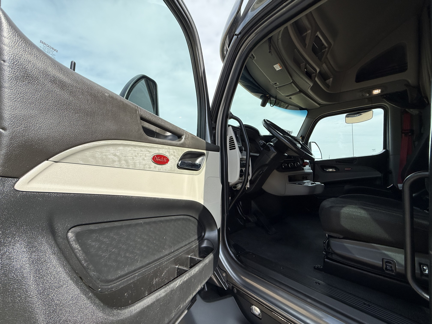 Peterbilt 579 truck interior view from open driver door showing steering wheel, dashboard, and seat with door panel visible.