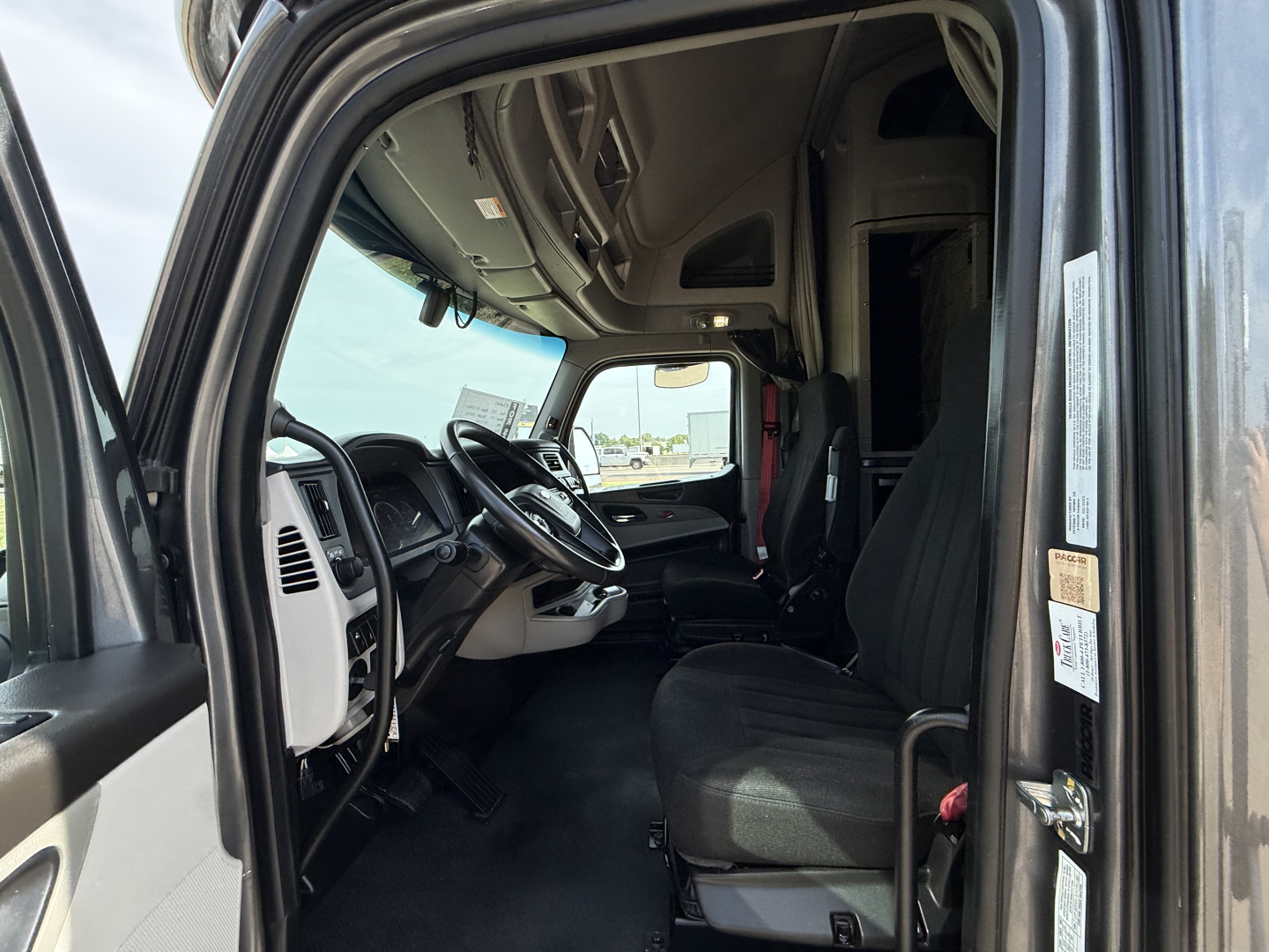 Peterbilt 579 truck cab interior view from open door showing steering wheel, dashboard, and driver's seat.