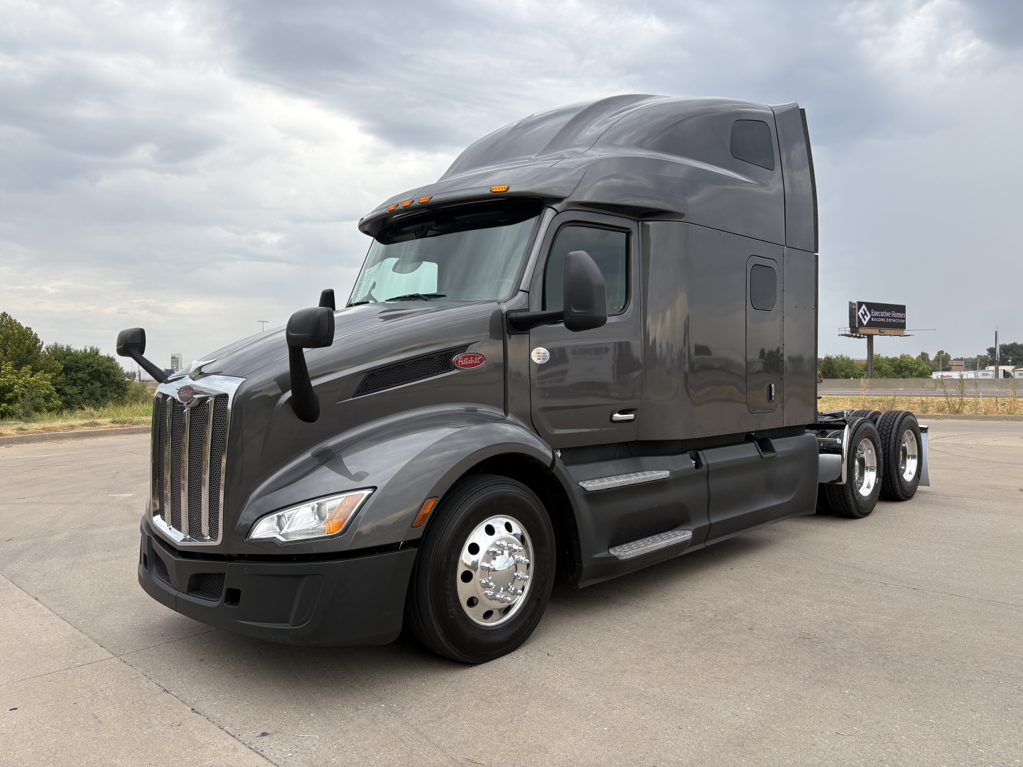 Peterbilt 579 truck in dark gray, semi-truck tractor with sleeper cab, front left view, chrome wheels, dual rear axles, daytime setting.
