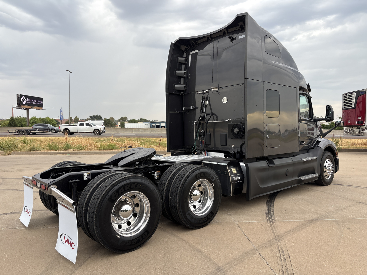 Peterbilt 579 sleeper tractor rear/side view showing chassis, dual rear axles, fifth wheel, and grey cab with exposed wiring and bumper markings.