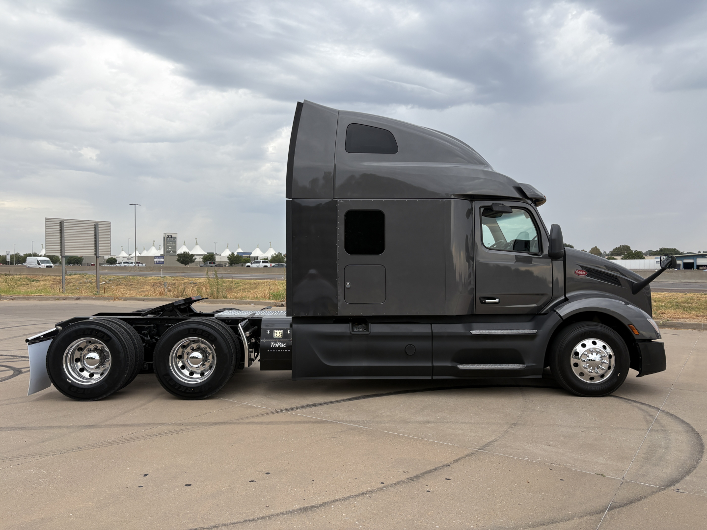 Peterbilt 579 truck side profile showing sleeper cab and three rear axles, black exterior, daytime sky.