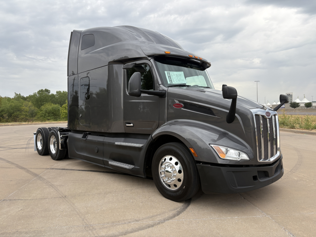Peterbilt 579 conventional sleeper tractor in dark gray, side view with sleeper cab, three axles, chrome wheels, daytime running lights.