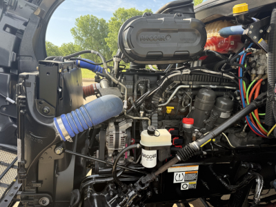 Peterbilt 579 engine bay with PACCAR-branded air intake, various hoses, hoses, and fluid reservoirs visible.