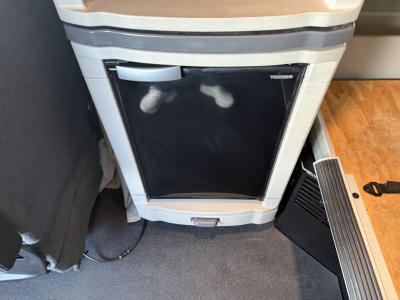 Refrigerator panel and interior in a Peterbilt 579 truck cab, showing a small fridge with black door and chrome handle, adjacent control panel area.