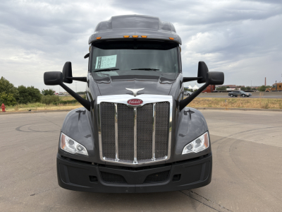 Peterbilt 579 conventional sleeper truck front view showing chrome grille, dual headlights, large cargo mirrors, and windshield with inspection sticker.