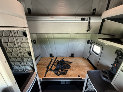 Peterbilt 579 sleeper cab interior cargo area showing wooden floor and storage shelves, with straps on the floor and side panels.