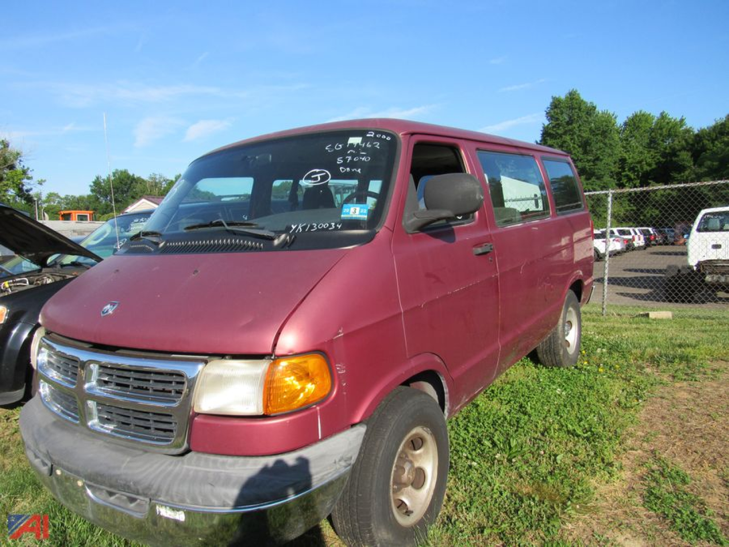 Dodge Ram full-size van with maroon exterior, side view showing front grille and passenger side, worn bumper, in a used vehicle lot.