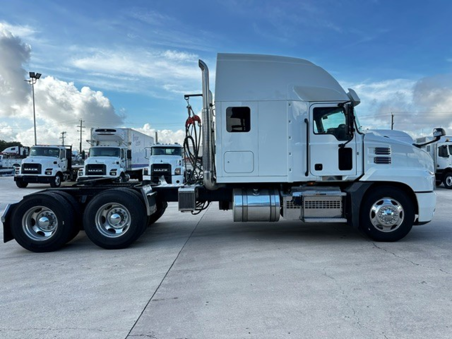 Truck showing side profile of a white Mack AN64T70 tractor with sleeper cab and chrome fuel tanks; multiple trailers in background.