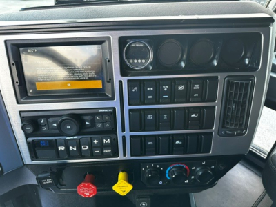 Mack AN64T70 truck dashboard with touchscreen display, various switches, gauges, and climate controls; gear selector shows R N D plus M; emergency/disconnect buttons visible.