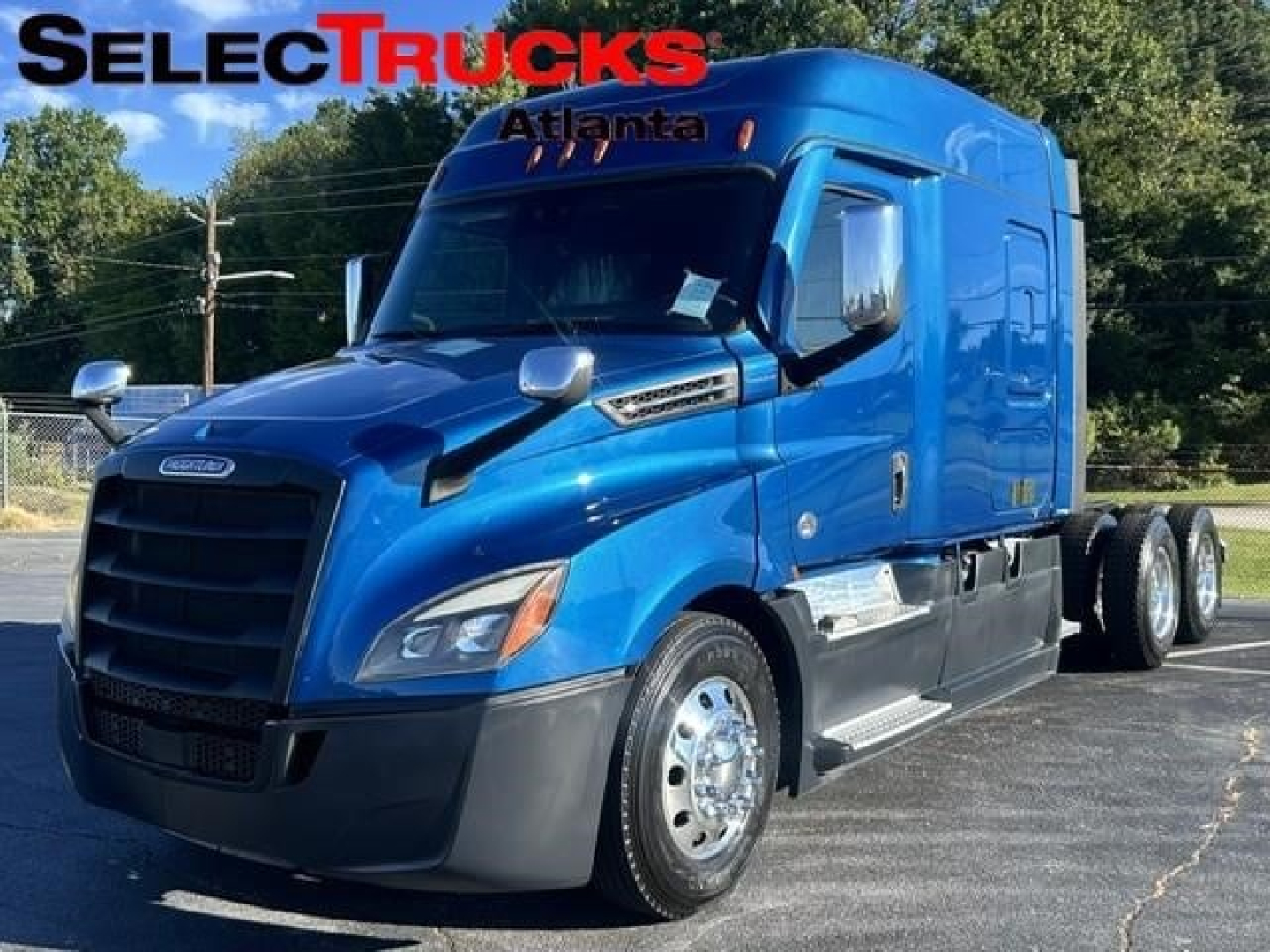 Blue Freightliner Cascadia 2022 sleeper cab truck with chrome wheels and dual rear axles in dealership lot.
