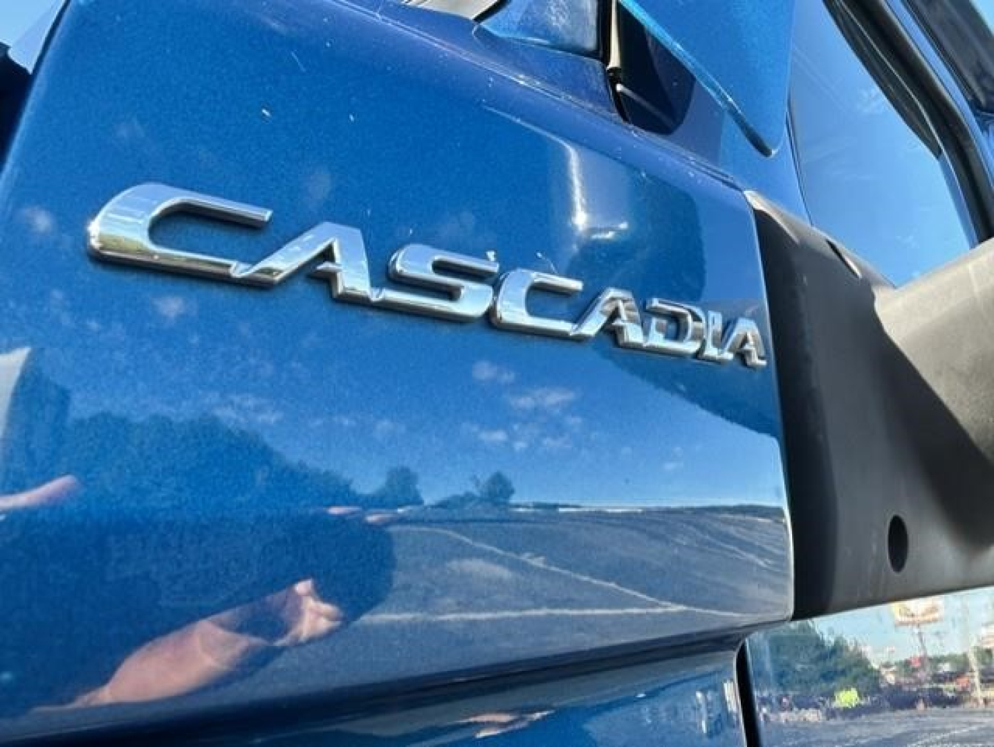 Freightliner Cascadia badge on blue truck door showing CASCADIA logo and side mirror.