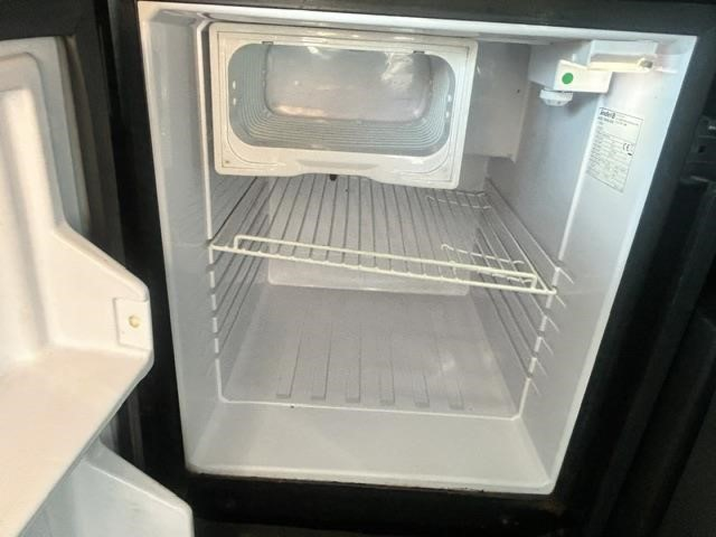 Freightliner Cascadia engine bay showing empty refrigerator-freezer compartment and storage shelf inside a side-by-side unit.