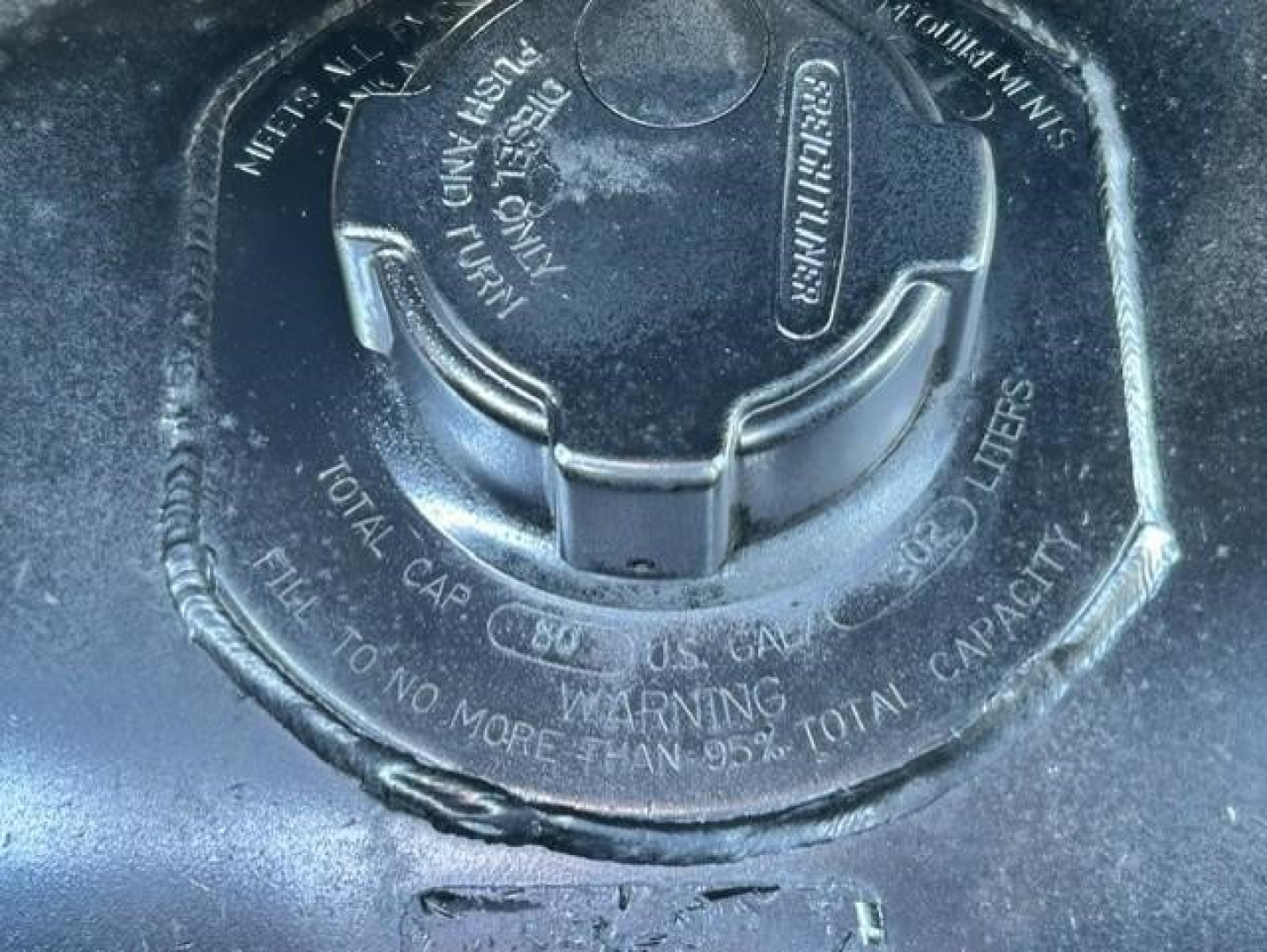 Fuel tank fill cap with embossed warnings and markings on a Freightliner Cascadia engine area showing cap and surrounding text