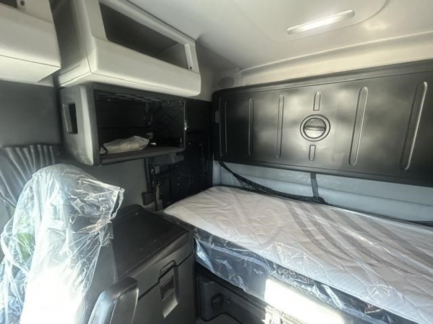 Freightliner Cascadia sleeper cab interior showing bunk bed with plastic-covered mattress and overhead storage shelf.