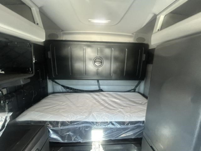 Cab interior of a 2022 Freightliner Cascadia sleeper truck showing a bunk bed area with a mattress and overhead storage cabinets.