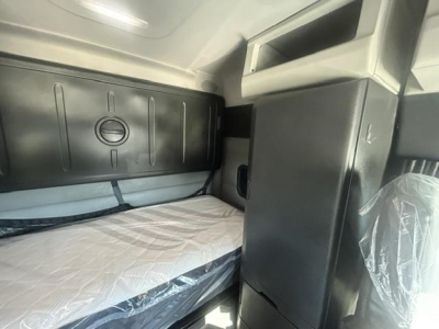Truck sleeper cab interior of a 2022 Freightliner Cascadia showing a bunk bed with protective plastic on the seat and storage cabinets.