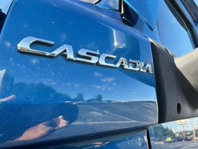 Freightliner Cascadia badge on blue truck door showing CASCADIA logo and side mirror.