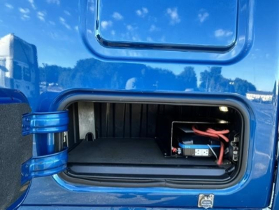 Freightliner Cascadia engine bay storage compartment showing battery pack and wiring inside side access compartment.