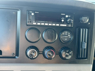 Freightliner Cascadia dashboard showing factory radio, circular gauges, climate controls, and power outlet. Visible text includes Power Outlet 110V and control buttons on radio panel.