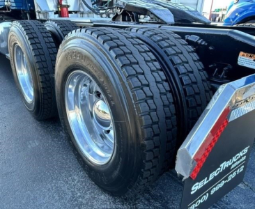 Freightliner Cascadia rear dual axle with heavy-duty tires and chrome rims; portion of trailer fender with reflective red-and-white stripe and plate reading SELECTTRUCKS