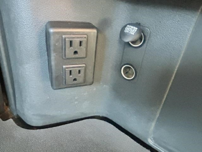 Freightliner Cascadia engine bay area showing dual power outlets and circular 12V auxiliary port with plastic cap.