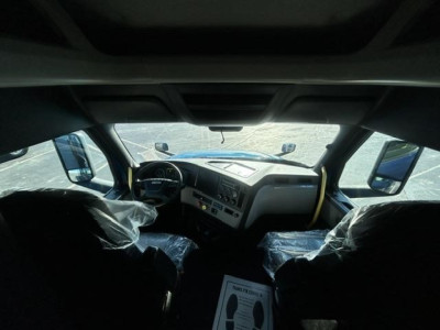 Freightliner Cascadia interior view showing steering wheel dashboard and driver seats wrapped in plastic.