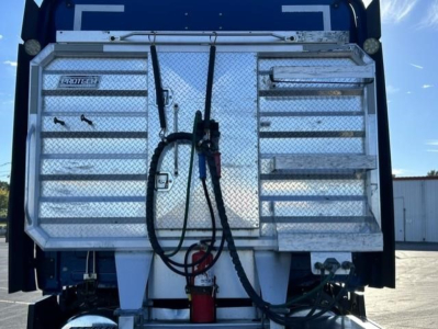 Rear view of a freight truck cargo area with fold-down aluminum toolbox doors, hoses, and a red fire extinguisher mounted beneath; diamond plate pattern and wiring visible.