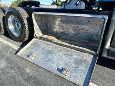 Freightliner Cascadia truck side box/compartment with open metal storage hatch showing interior, wheel and chassis in background.