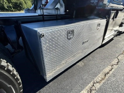 Aluminum diamond plate toolbox mounted on the side of a Freightliner Cascadia truck, reflective surface with a latch handle and a small lock hole.