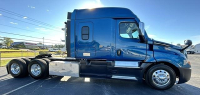 Freightliner Cascadia truck side view showing blue sleeper cab and dual rear axles with chrome wheels.