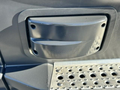 Freightliner Cascadia step area with grab handle and perforated metal step showing a few screws and circular holes.