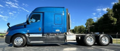 Truck side view of a blue 2022 Freightliner Cascadia sleeper tractor showing chassis and wheels with triple rear axles.