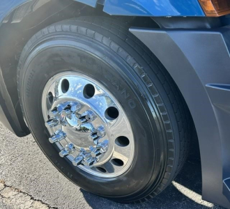 Truck wheel close-up showing chrome hubcap, black tire, and blue fender of a Freightliner Cascadia.