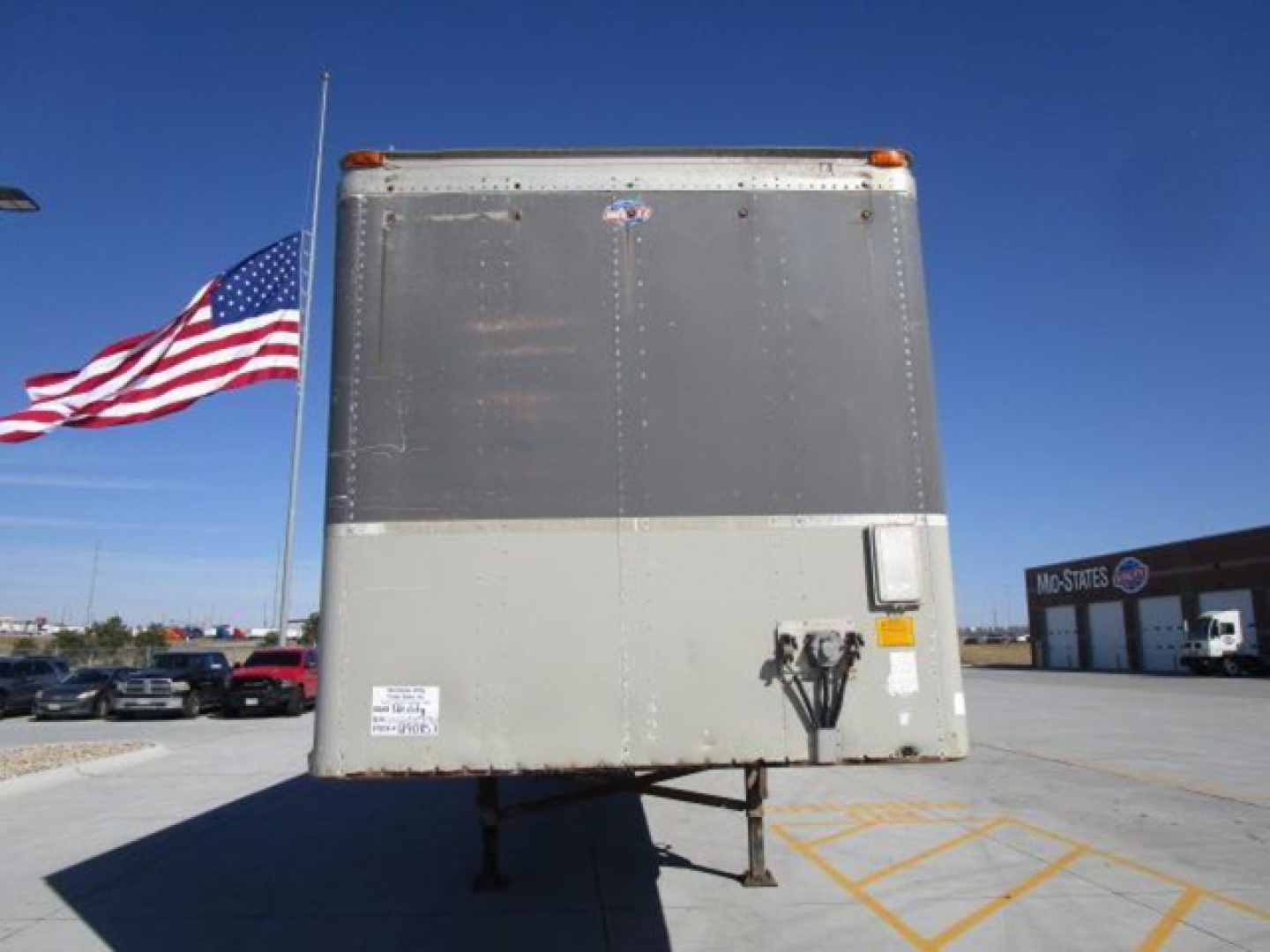 Trailer rear showing vertical riveted metal door and support legs with small sticker and latch.
