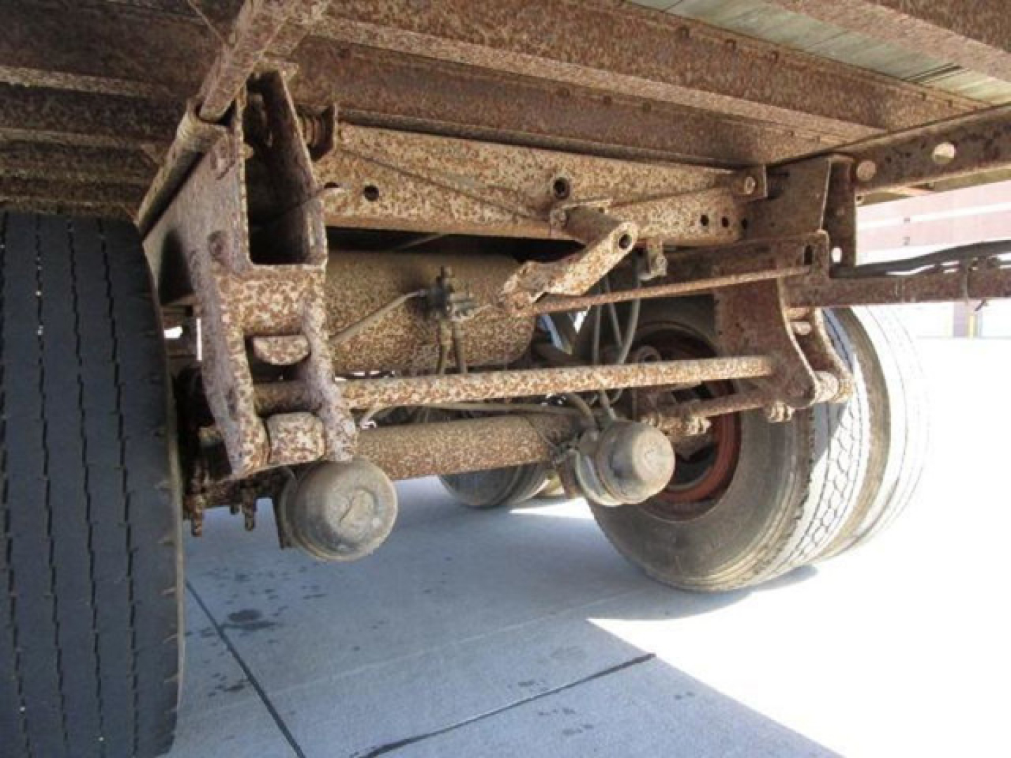 Under-axle view of a utility van showing rusted suspension and dual rear wheels with leaf springs and axles.