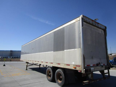 Trailer side view showing utility van/trailer with dual rear wheels, silver side panels, rear doors, and reflective tape.