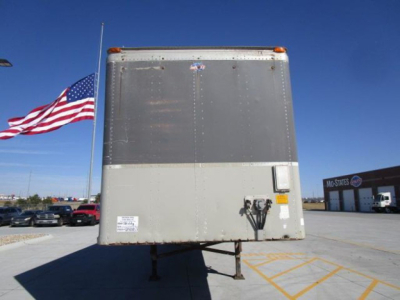 Trailer rear showing vertical riveted metal door and support legs with small sticker and latch.