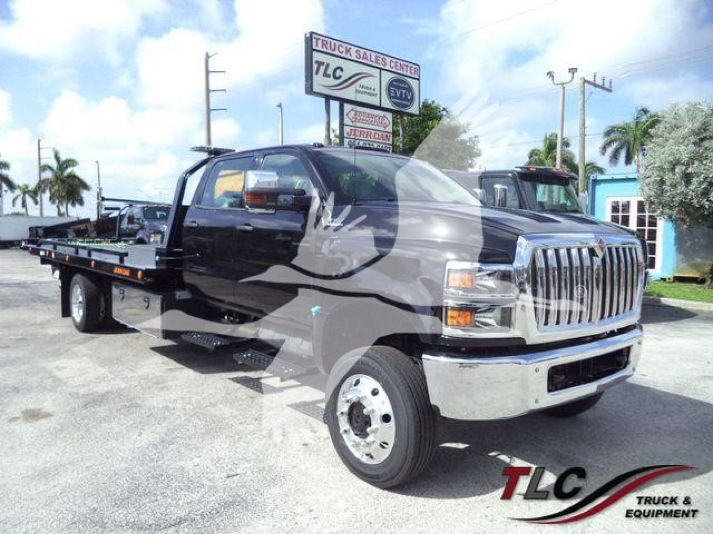 Truck with flatbed tow body in a dealership lot, International CV cargo/tow truck visible with chrome front grille and large side mirrors.