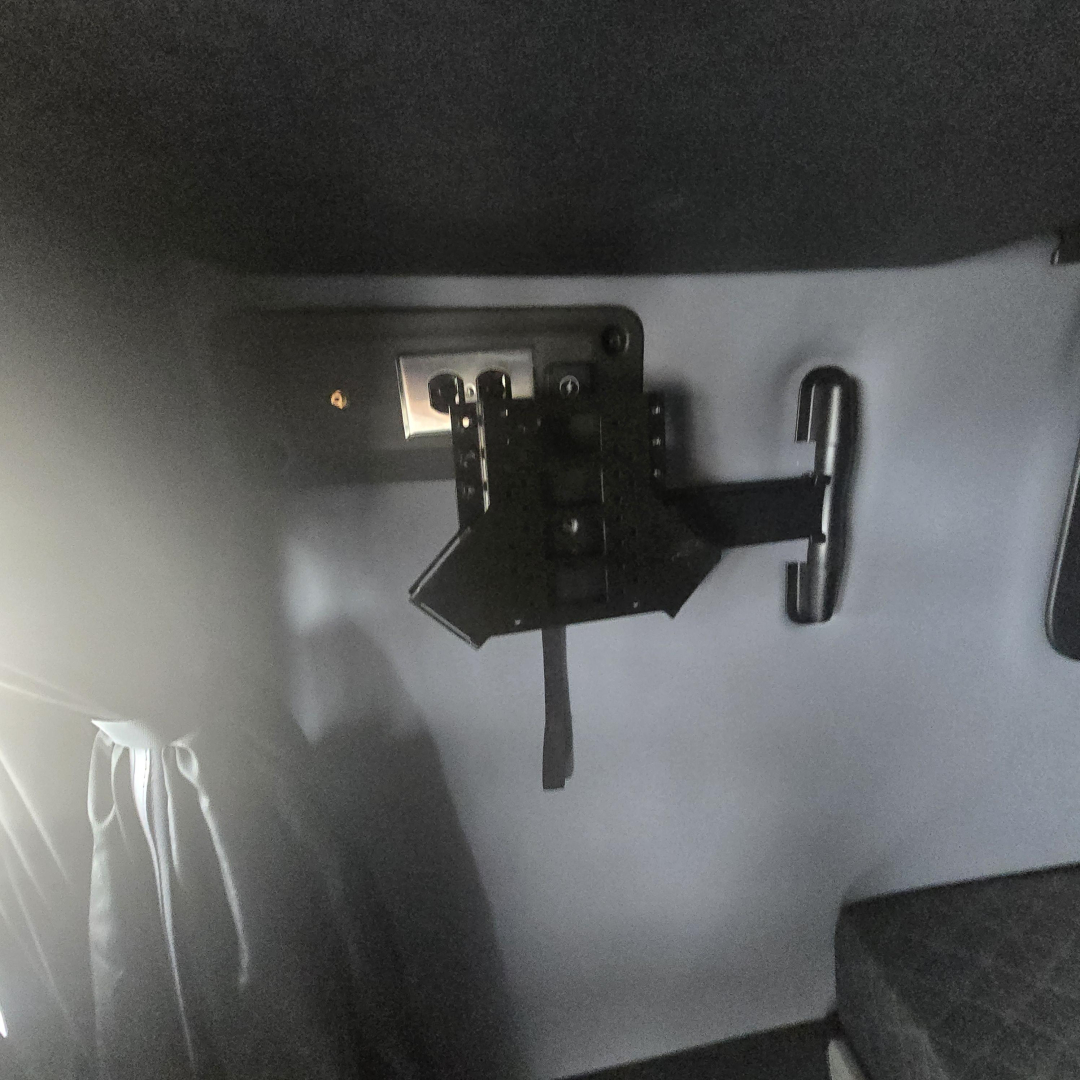 Trailer/vehicle interior showing a black mounting bracket and a handle on a grey wall, with a white plate and small screws visible.