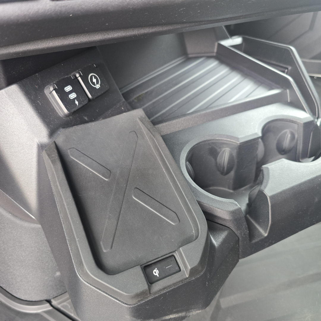 Inside cabin center console of a 2026 Mack PR64T76M showing cup holders, storage bin, and a small switch adjacent to a USB-like port.