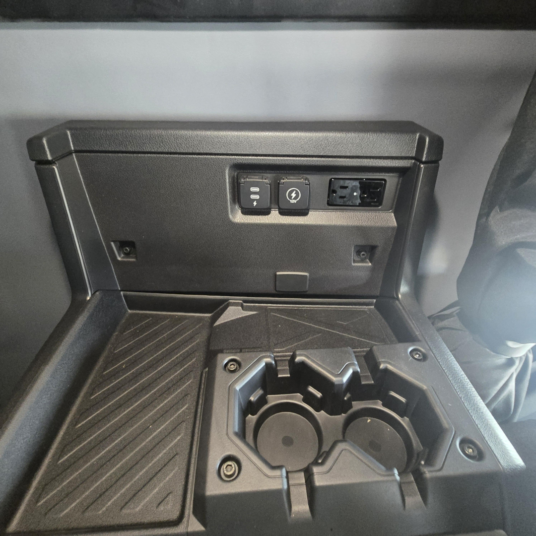 Dashboard area of a new Mack PR64T76M showing cupholders and control panel with 12V/USB ports and power outlet.