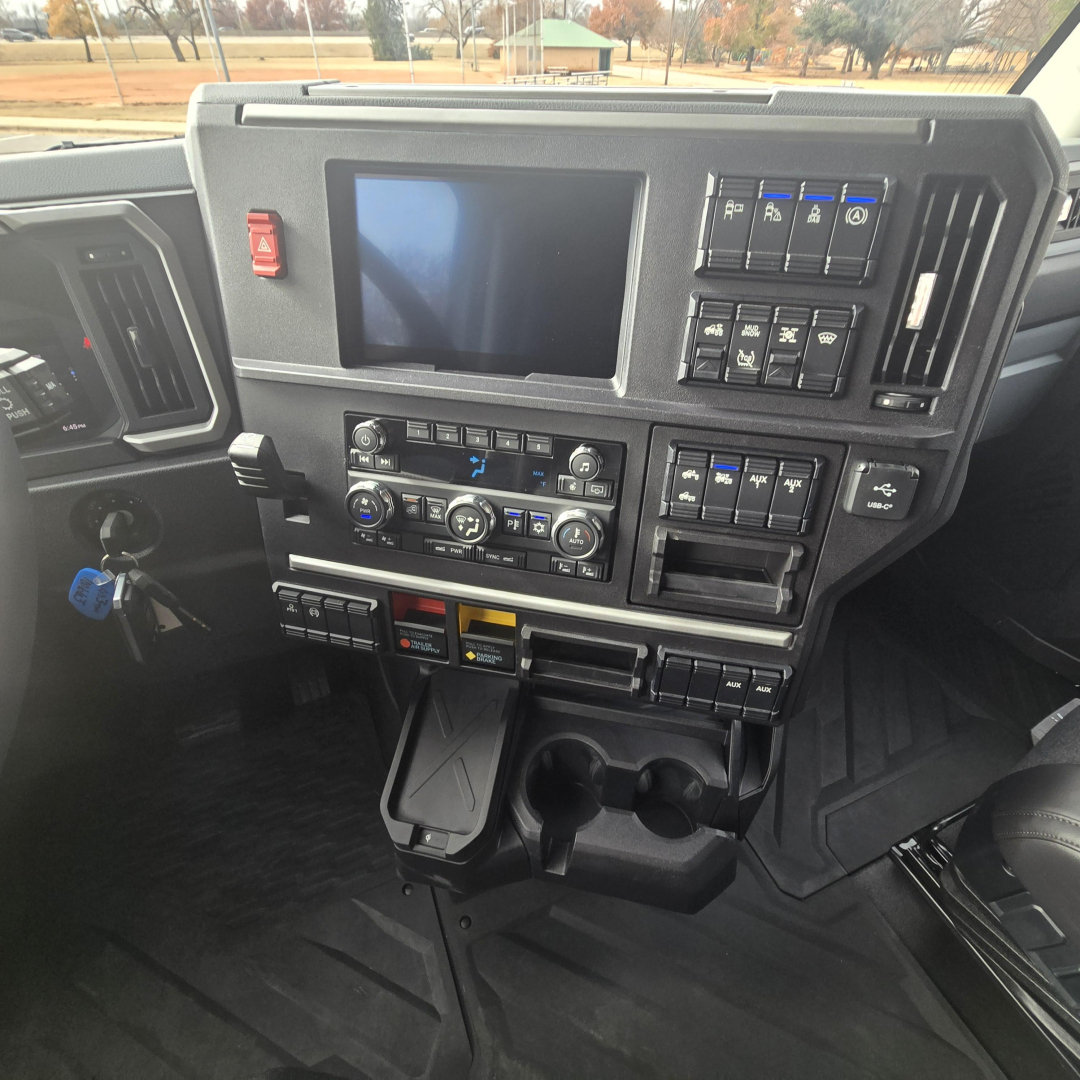 Dashboard of a 2026 Mack PR64T76M truck showing multiple control clusters, touchscreen display, vertical switches, gear levers, and cup holders.