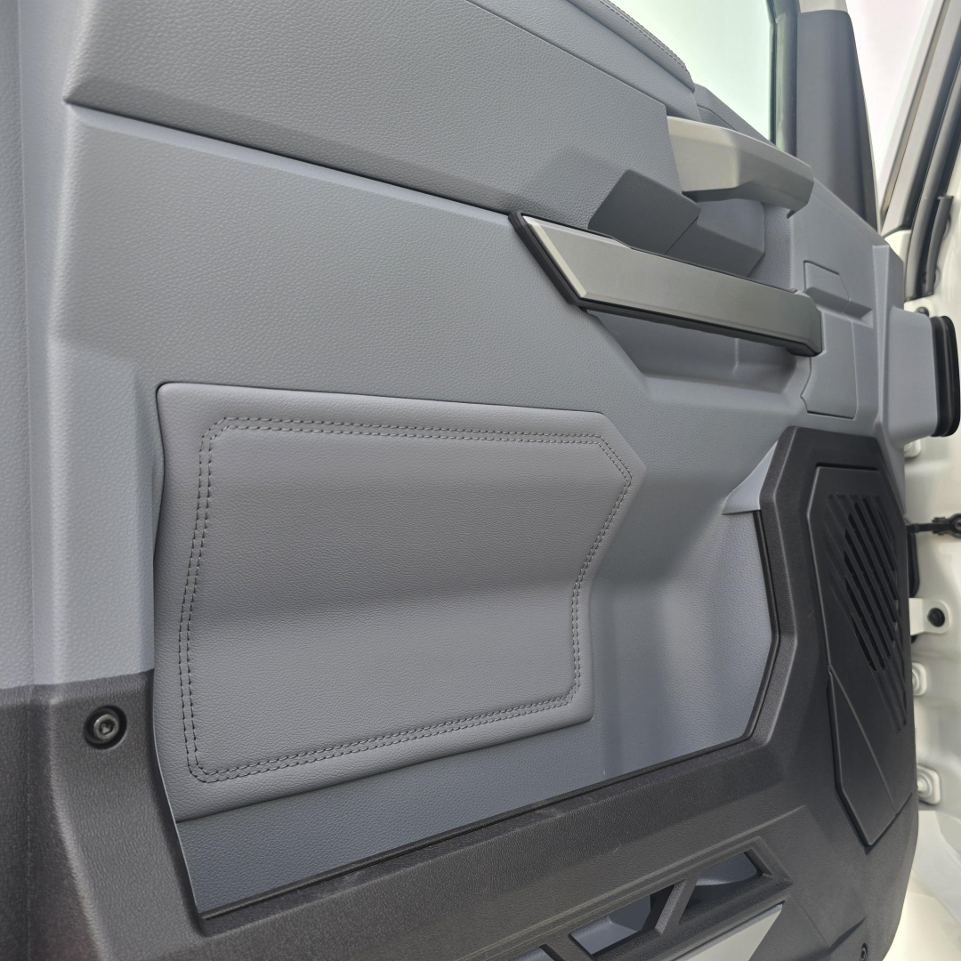 Truck cab interior door panel with light gray upholstery and black handle, side view showing storage pocket and speaker grille.