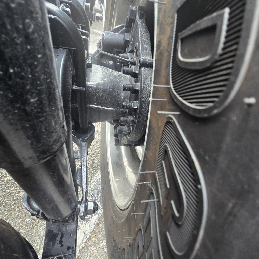 Truck wheel and suspension components with heavy-duty hub, brake drum, and tire profile visible; close-up view of the front axle area.