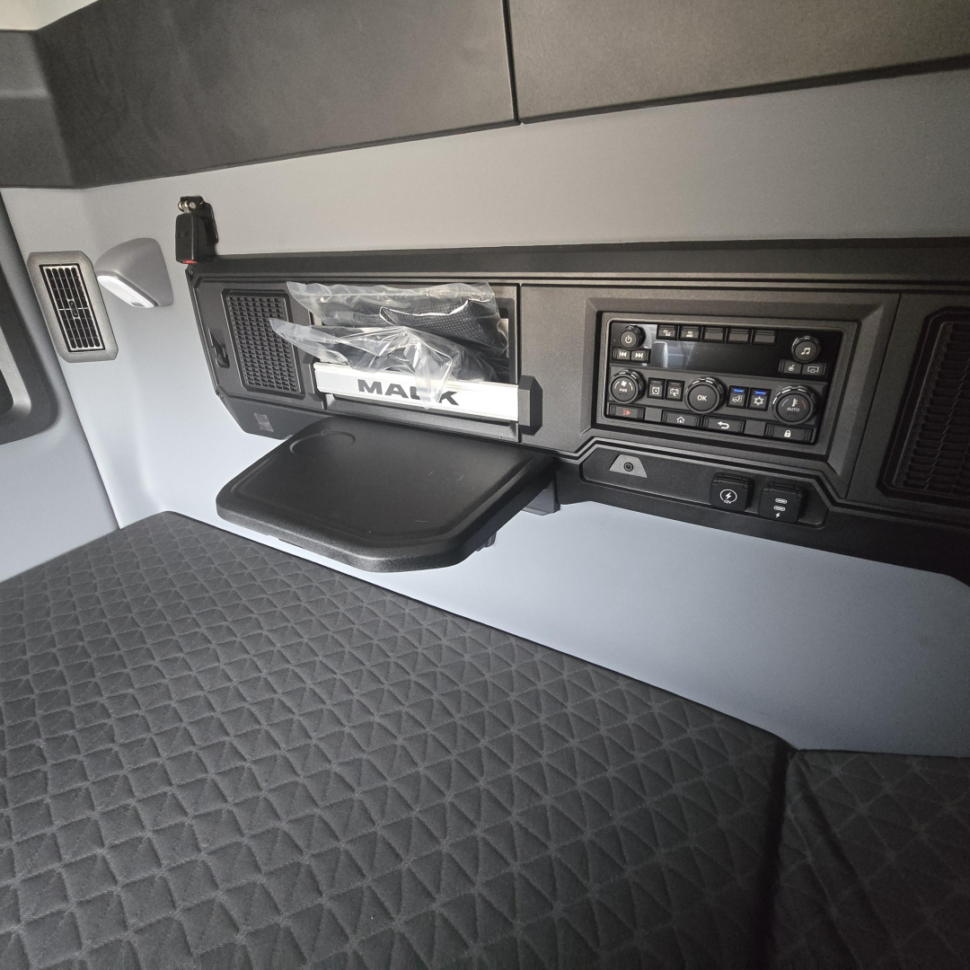 Mack PR64T76M truck interior dashboard and sleeper area showing control panel, storage pocket, and quilted seat/bed area.
