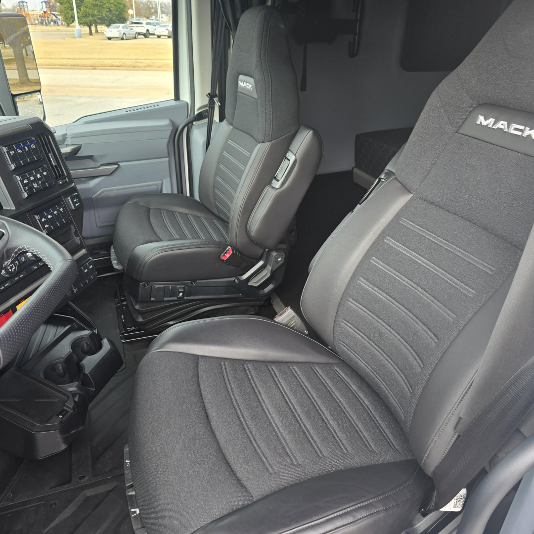 Interior of a 2026 Mack PR64T76M truck cab showing driver and passenger seats with Mack branding on headrests and dashboard controls visible.