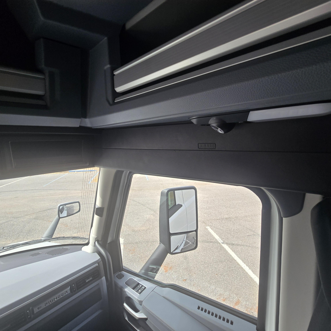 Cab interior of a new Mack PR64T76M truck showing dash and large side mirror, overhead storage, and a forward view through the windshield.