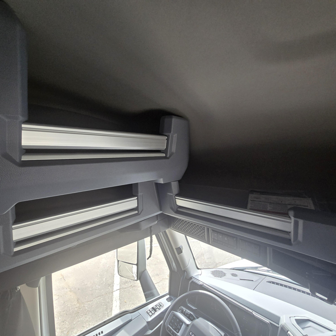 Cab interior overhead storage compartments in a Mack PR64T76M truck cab showing open lids and storage rails.