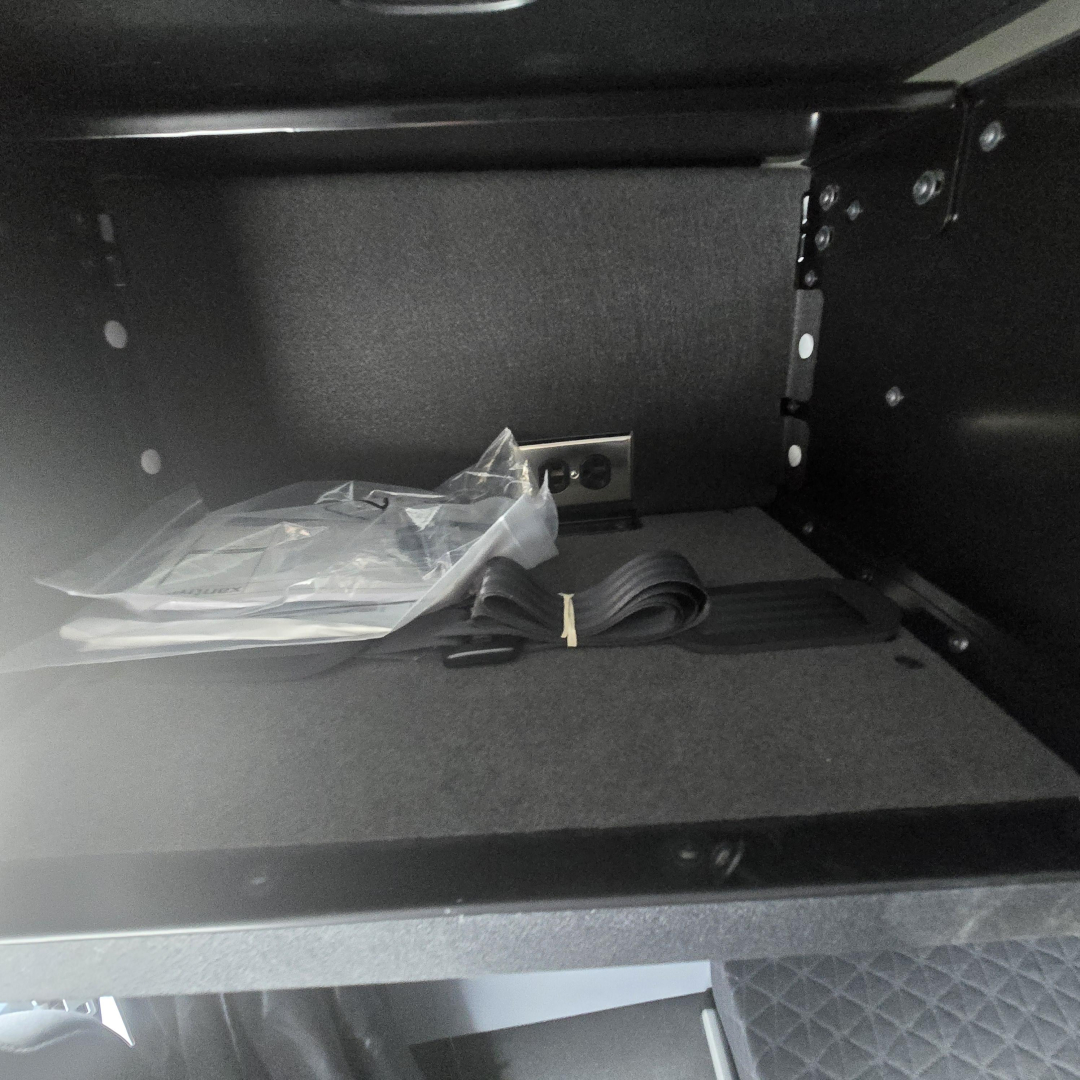 Cab interior storage drawer with strap and small plastic bag inside.